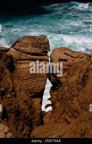 Arancione e turchese: Surf Atlantico schiumoso visto attraverso le lacune tra due falde calcaree stagionato e scagliante sotto scogliere scoscese sulla costa di Cabo Carvoeiro a Peniche nel distretto di Leiria, Portogallo centrale. Molte delle pile e dei pilastri del mare aperto sono scolpiti dal vento e dalle onde in forme strane e curiose. Foto Stock