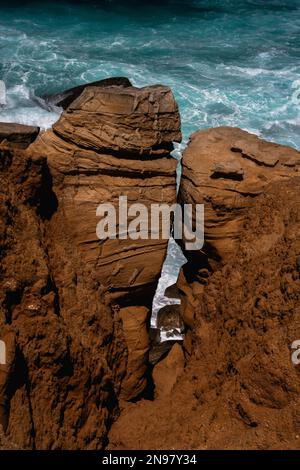 Frottatura e sfaldatura: Surf Atlantico schiumoso visto attraverso le lacune tra due falde calcaree stagionate e sbriciolanti sotto scogliere scoscese sulla costa di Cabo Carvoeiro a Peniche nel distretto di Leiria, Portogallo centrale. Molte delle pile e dei pilastri del mare aperto sono scolpiti dal vento e dalle onde in forme strane e curiose. Foto Stock