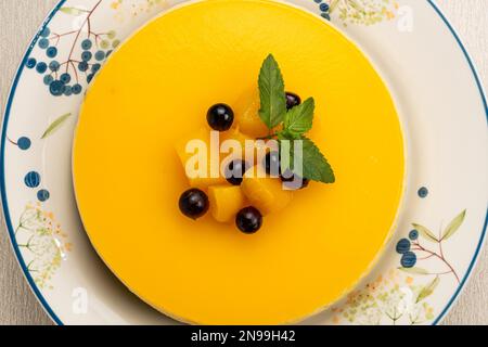Vista dall'alto di una deliziosa cheesecake fatta in casa con pezzi di pesca, mirtillo e foglia di menta verde conservati in piatto di ceramica bianca Foto Stock