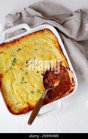 Piatto tradizionale di cucina britannica Pastore torta casseruola con carne tritata e purè di patate in ceramica da forno piatto su bianco tavolo rustico con Foto Stock