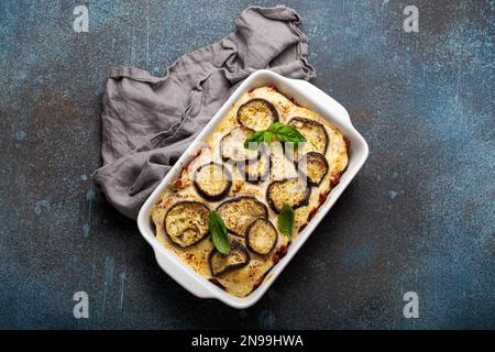 Piatto greco mediterraneo Moussaka con melanzane al forno, macinato di manzo in casseruola bianca in ceramica su sfondo rustico di pietra dall'alto, tradizionale Foto Stock