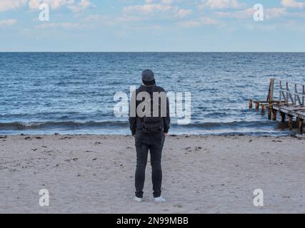 vista posteriore dell'uomo che indossa felpa con cappuccio e jeans guardando il mare Foto Stock