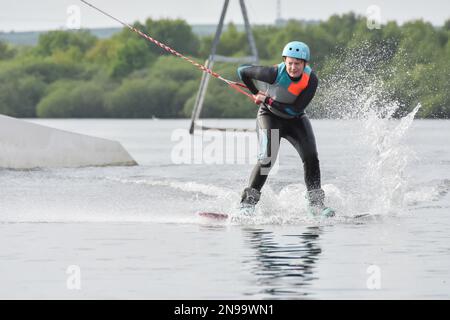 Staffordshire, Regno Unito. Maggio 2018. Wakeboarder surf attraverso il lago utilizzando un cavo di traino Foto Stock