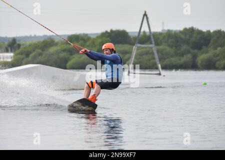 Staffordshire, Regno Unito. Maggio 2018. Wakeboarder surf attraverso il lago utilizzando un cavo di traino Foto Stock