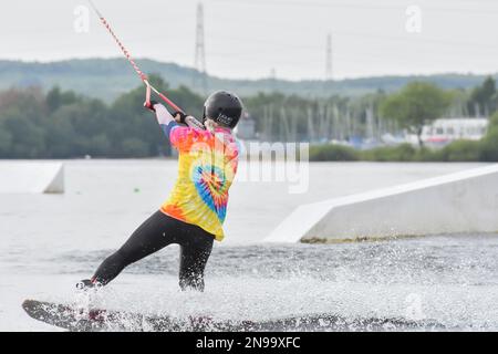 Staffordshire, Regno Unito. Maggio 2018. Wakeboarder surf attraverso il lago utilizzando un cavo di traino Foto Stock