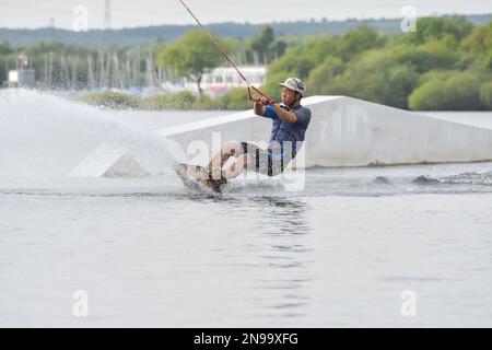 Staffordshire, Regno Unito. Maggio 2018. Wakeboarder surf attraverso il lago utilizzando un cavo di traino Foto Stock