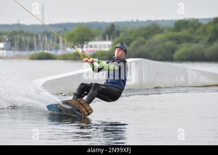 Staffordshire, Regno Unito. Maggio 2018. Wakeboarder surf attraverso il lago utilizzando un cavo di traino Foto Stock