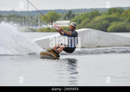 Staffordshire, Regno Unito. Maggio 2018. Wakeboarder surf attraverso il lago utilizzando un cavo di traino Foto Stock