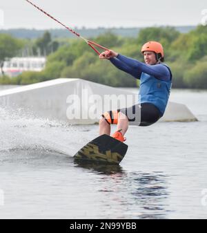 Staffordshire, Regno Unito. Maggio 2018. Wakeboarder surf attraverso il lago utilizzando un cavo di traino Foto Stock