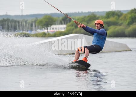 Staffordshire, Regno Unito. Maggio 2018. Wakeboarder surf attraverso il lago utilizzando un cavo di traino Foto Stock