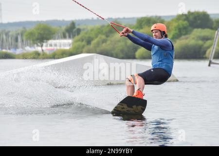 Staffordshire, Regno Unito. Maggio 2018. Wakeboarder surf attraverso il lago utilizzando un cavo di traino Foto Stock