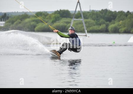 Staffordshire, Regno Unito. Maggio 2018. Wakeboarder surf attraverso il lago utilizzando un cavo di traino Foto Stock