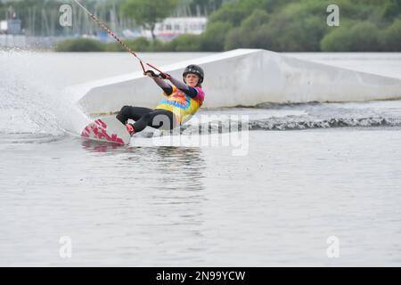 Staffordshire, Regno Unito. Maggio 2018. Wakeboarder surf attraverso il lago utilizzando un cavo di traino Foto Stock