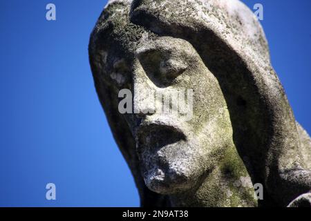 Primo piano faccia di Gesù Cristo crollando muschio coperto statua di pietra cimitero. Messa a fuoco selettiva, sfondo cielo blu. Foto Stock