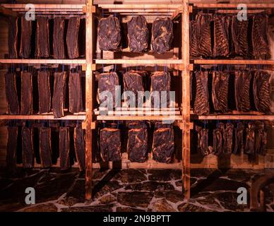 Varie specialità di carne tirolese affumicata appendono nella sala di essiccazione Foto Stock