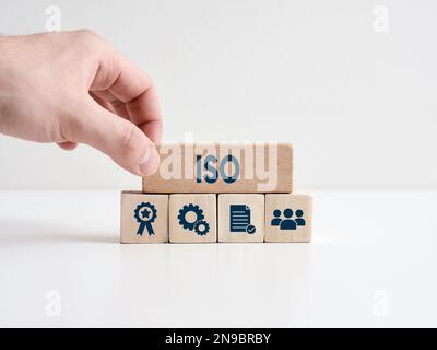 Standard ISO controllo qualità, garanzia e certificazione di garanzia. La mano posiziona il blocco di legno con la parola ISO sui cubi con Internationa Foto Stock