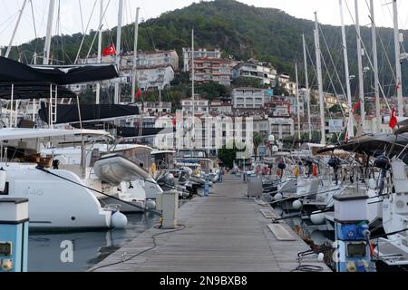 Fethiye, Turchia, 9 novembre 2022: Barche e navi a vela si trovano nel porto turistico sullo sfondo di edifici residenziali della città. Un pi. In legno Foto Stock