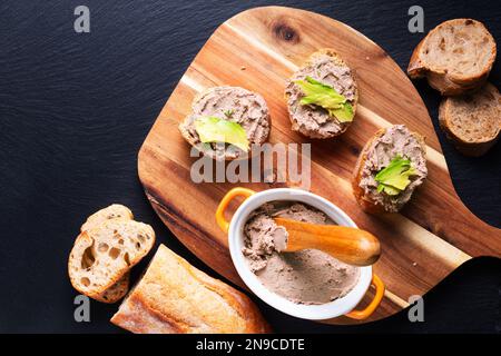 Concetto alimentare Pollo fegato spalmato Pate Baguette morso su tavola di legno su sfondo nero con spazio copia Foto Stock