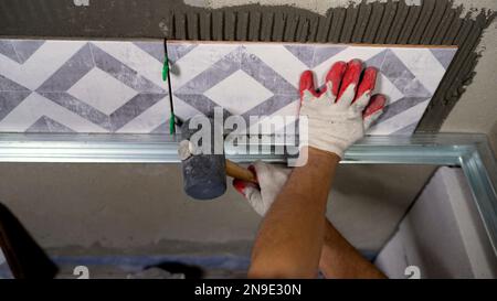 Installazione di piastrelle in ceramica. Le mani maschili incollano le piastrelle di ceramica sulla parete del bagno. Foto Stock