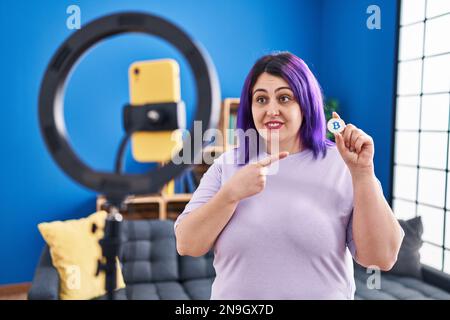 Plus size wit wit porpora registrazione capelli bitcoin tutorial con smartphone a casa sorridente felice puntamento con mano e dito Foto Stock