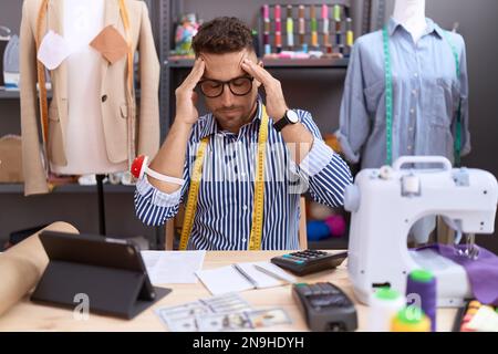 Uomo ispanico con Beard dresssaker designer che lavora presso atelier con mano sulla testa, mal di testa perché stress. emicrania sofferente. Foto Stock