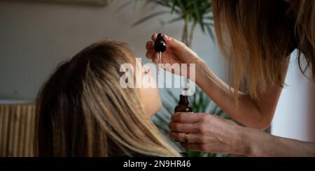 Vista di primo piano di una madre che dà al suo bambino gocce di vitamina, medicina o integratore alimentare con un contagocce. Foto Stock