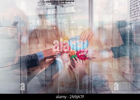 Il team aziendale collega pezzi di attrezzi colorati come un lavoro di squadra e partner sullo sfondo degli edifici cittadini Foto Stock