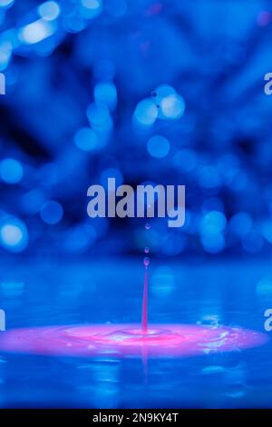 Una goccia cade in un liquido spesso con uno sfondo blu-rosa. Sfondo colorato astratto Foto Stock