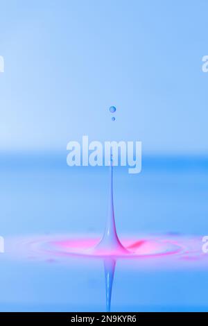 Una goccia cade in un liquido spesso con uno sfondo blu-rosa. Sfondo colorato astratto Foto Stock