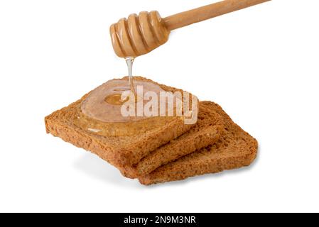 Miele d'acacia che sgocciola dal cucchiaiato di miele sulle fette di pane tostato, isolato su bianco, percorso di taglio Foto Stock