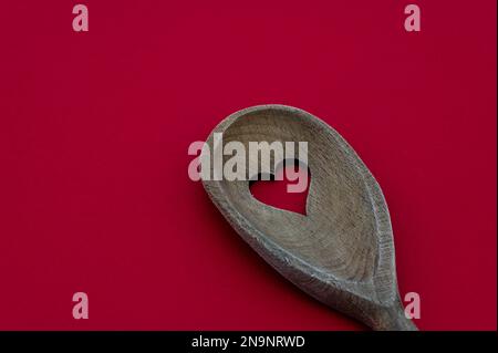 Cucchiaio di legno con foro a forma di cuore isolato su fondo rosso. Concetto di cucina e salute Foto Stock