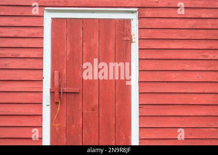 Primo piano di una porta di legno in una pescheria rossa con lati di legno; Battle Harbour, Terranova e Labrador, Canada Foto Stock