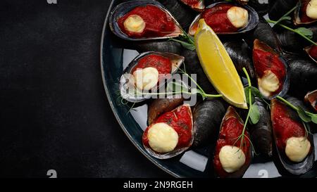 cozze bollite con formaggio e salsa di pomodoro piccante in un piatto scuro, su cemento scuro Foto Stock