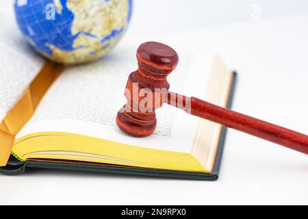 Il libro con i bordi dorati, il gavel di legno ed il globo disposto sul fondo bianco tiene i concetti globali di equità e di giustizia Foto Stock