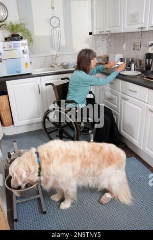 Donna disabile in sedia a rotelle in cucina con il suo cane Foto Stock