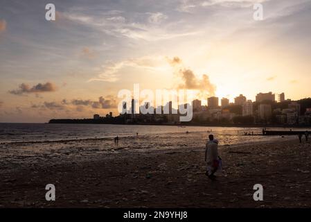 Persone a Chowpatty Beach al tramonto con vista sullo skyline di Mumbai; Mumbai, Maharashtra, India Foto Stock