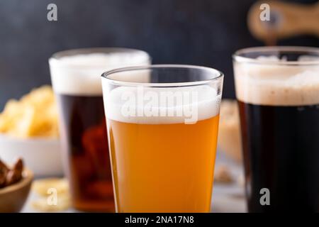 Varietà di birra con stout scuro, lager tradizionale e bianco belga servito con spuntini sul tavolo Foto Stock