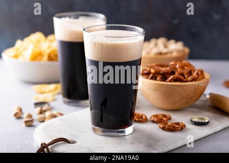 Birra scura in bicchieri alti, birra e spuntini sul tavolo Foto Stock