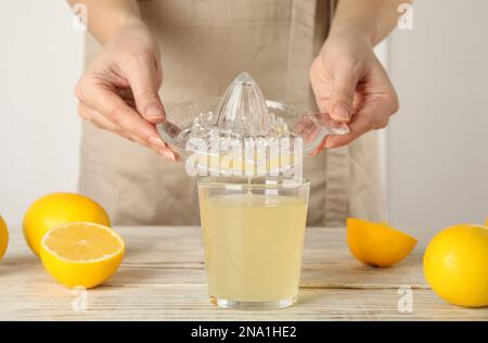 Donna che versa succo di limone spremuto fresco in vetro a tavola di legno bianco, primo piano Foto Stock