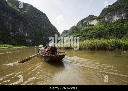 Persone in una barca sul fiume Dong ONG circondato da montagne carsiche di pietra calcarea; Tam Coc, Ninh Binh, Vietnam Foto Stock