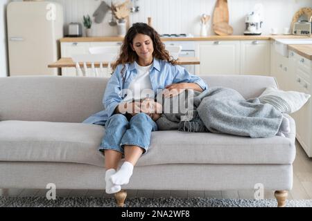 Figlia stanca coperta di coperta calda addormentarsi dopo la scuola, dormendo sulle ginocchia della madre Foto Stock