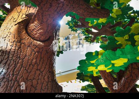 Guardando attraverso il gigantesco albero Lego, madre e figlia salgono le scale della casa Lego; Billund, Danimarca Foto Stock