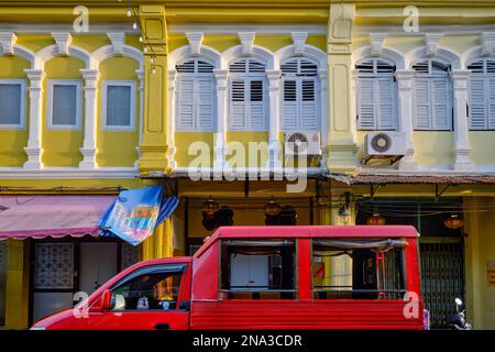 Colorate botteghe in stile sino-portoghese, con finestre ad arco e a graticcio, nella zona della Città Vecchia di Phuket, Thailandia; un tuk-tuk o un songthaew nel f/g. Foto Stock