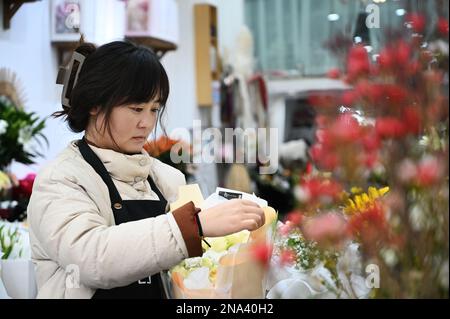 XUZHOU, CINA - 13 FEBBRAIO 2023 - un dipendente seleziona, organizza e confeziona i fiori in base a un ordine in un negozio di fiori nella contea di Suining, Xuzho Foto Stock