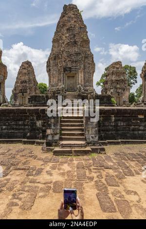 Donna con mobili fotografare il tempio in pietra rovinata, East Mebon, Angkor Wat; Siem Reap, provincia di Siem Reap, Cambogia Foto Stock