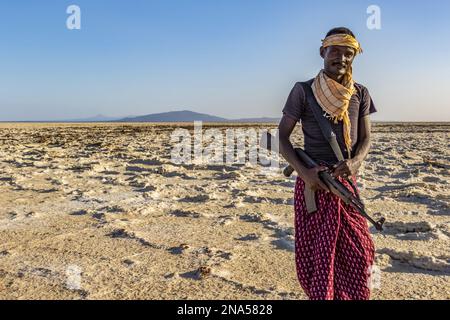 Lontano da un uomo che porta una pistola nelle distese saline del lago Karum (lago Assale), depressione Danakil; regione di Afar, Etiopia Foto Stock
