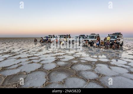 I turisti di fronte a un veicolo a quattro ruote motrici sulle distese saline del lago Karum (lago Assale) al tramonto, depressione Danakil; regione di Afar, Etiopia Foto Stock