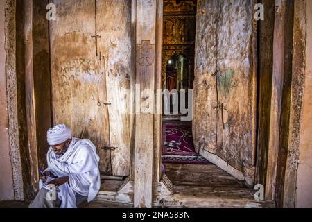 Sacerdote etiope ortodosso all'ingresso di Abreha WE Atsbeha roccia-scavata chiesa, Tigray, Etiopia Foto Stock