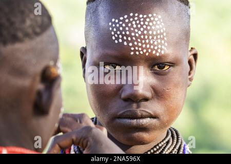 Il giovane Karo si fa decorare il viso con la tradizionale pittura del viso al villaggio di Kortcho, nella valle di Omo, Etiopia Foto Stock