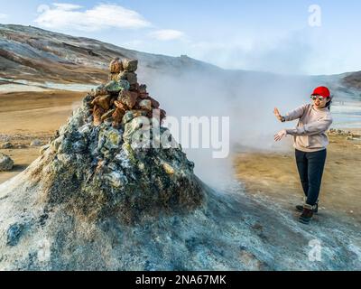 Una turista femminile si trova ai margini di una fumarola per sentire il vapore. Questo luogo geotermico è noto per le sue gorgoglianti piscine di fango e fumante fuma... Foto Stock